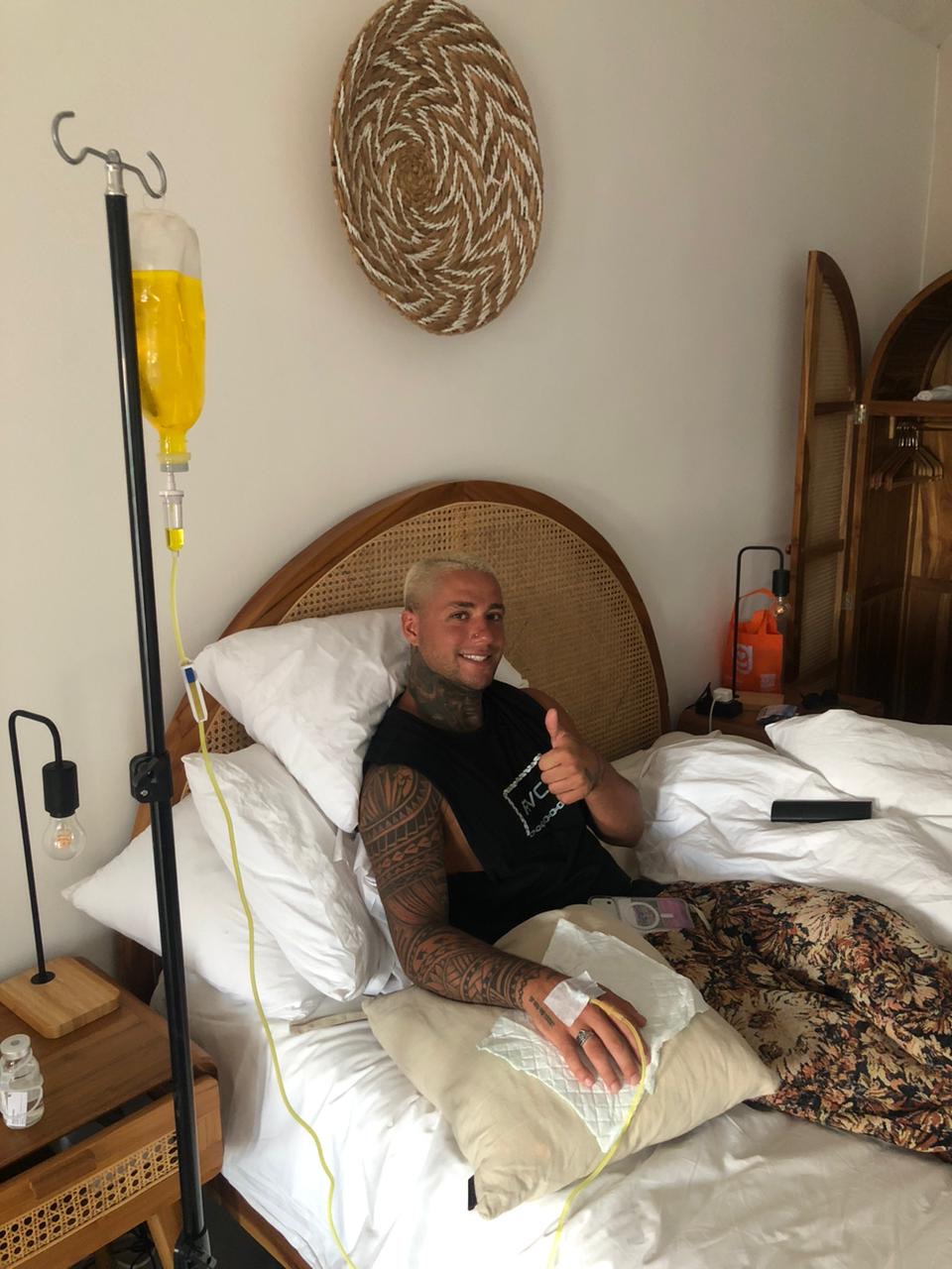 Man with tattoos receiving a mobile IV drip treatment while resting in a Bali villa bed.
