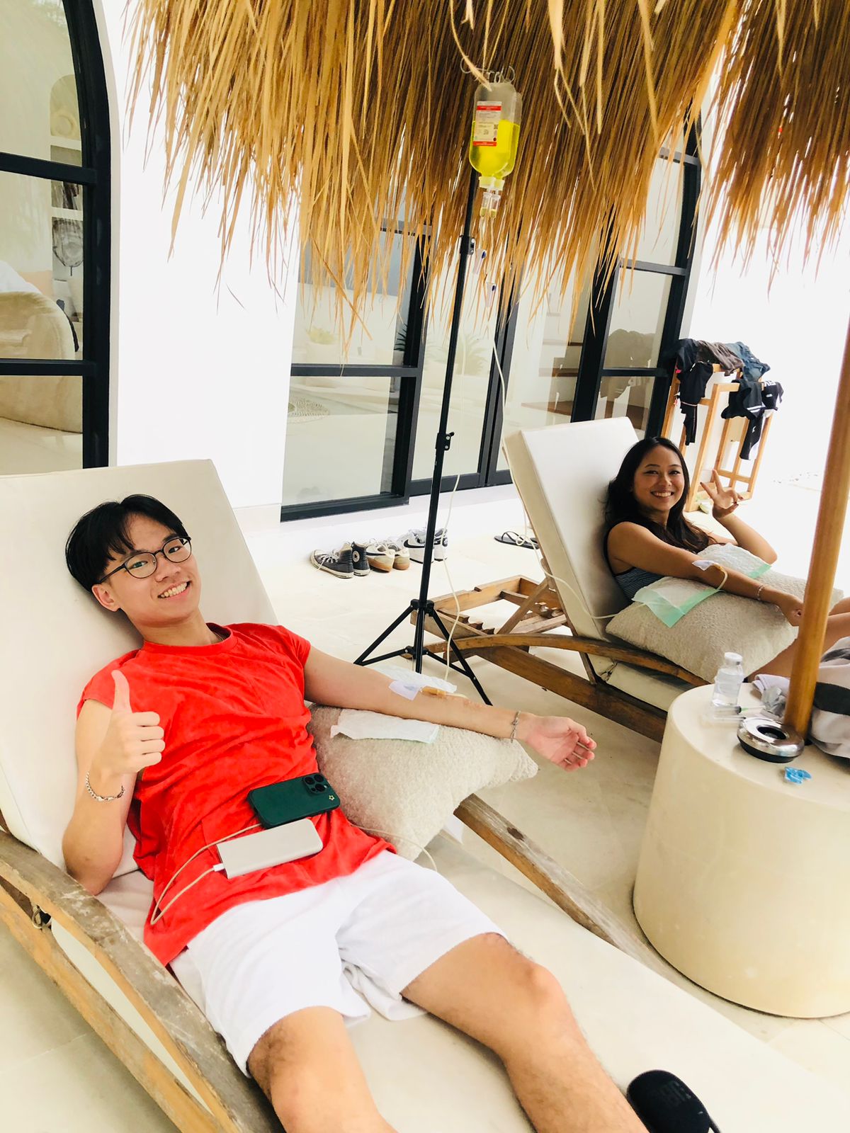 A couple relaxing on sun loungers receiving mobile IV drip therapy at a Bali villa.