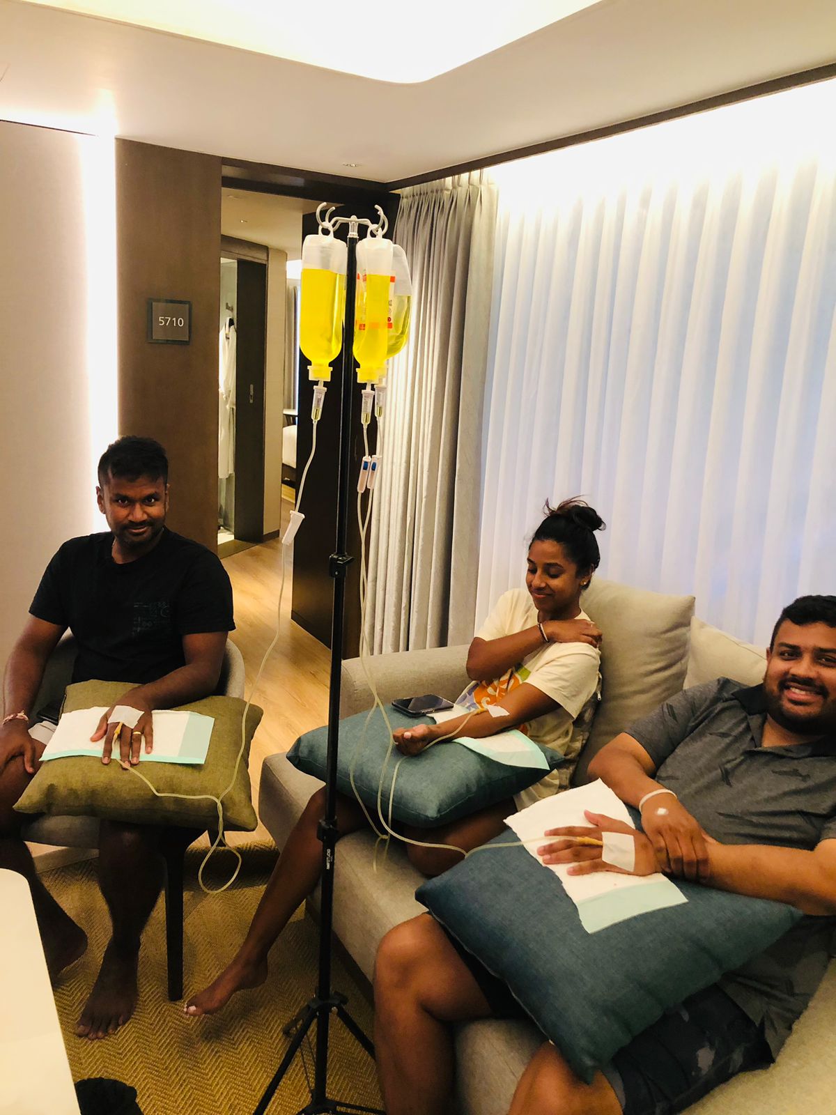 Three people receiving mobile IV drip hydration treatments while relaxing in a villa lounge.